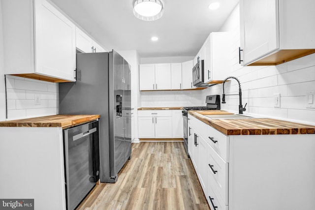 kitchen featuring stainless steel appliances, white cabinets, wooden counters, and light hardwood / wood-style floors