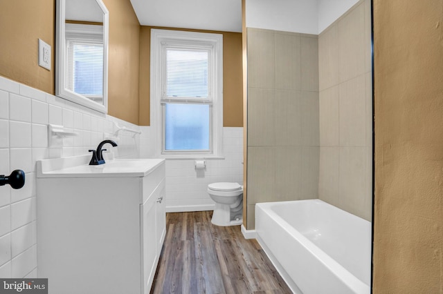 bathroom featuring a washtub, vanity, hardwood / wood-style flooring, tile walls, and toilet