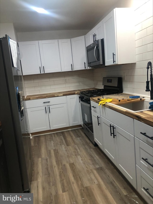 kitchen featuring dark wood-type flooring, decorative backsplash, appliances with stainless steel finishes, butcher block countertops, and white cabinetry