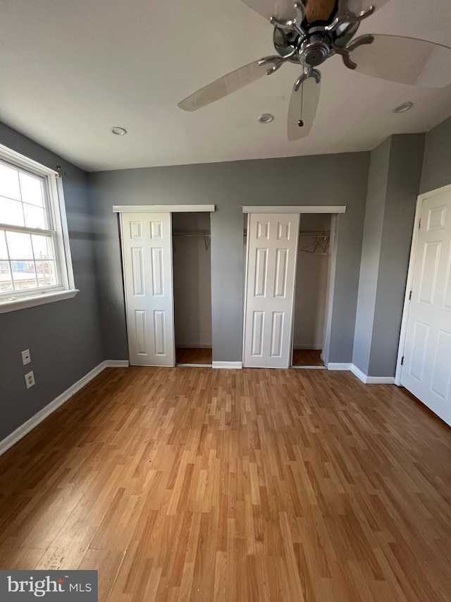 unfurnished bedroom featuring hardwood / wood-style flooring, ceiling fan, and multiple closets