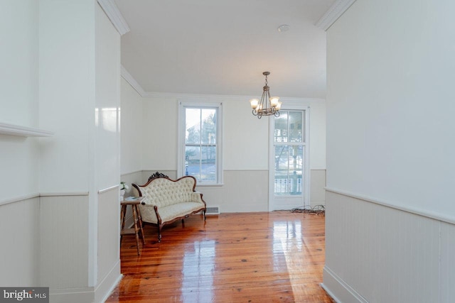 living area with crown molding, hardwood / wood-style floors, and an inviting chandelier