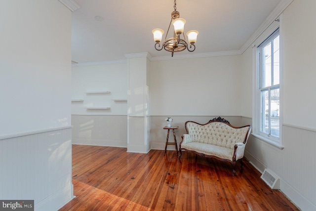 living area with hardwood / wood-style flooring, ornamental molding, and a chandelier