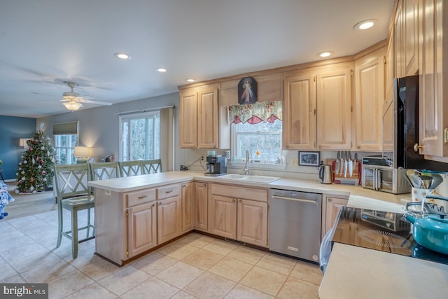 kitchen featuring a breakfast bar, sink, light brown cabinets, stainless steel dishwasher, and kitchen peninsula