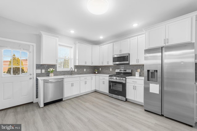 kitchen featuring white cabinetry, sink, stainless steel appliances, backsplash, and light wood-type flooring