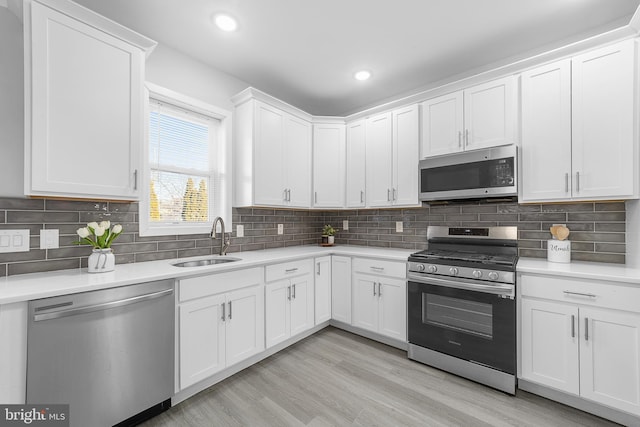 kitchen with sink, decorative backsplash, light wood-type flooring, white cabinetry, and stainless steel appliances