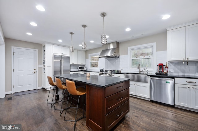 kitchen with stainless steel appliances, sink, wall chimney range hood, a center island, and white cabinetry