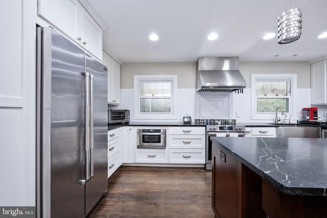 kitchen featuring wall chimney exhaust hood, stainless steel appliances, backsplash, pendant lighting, and white cabinets