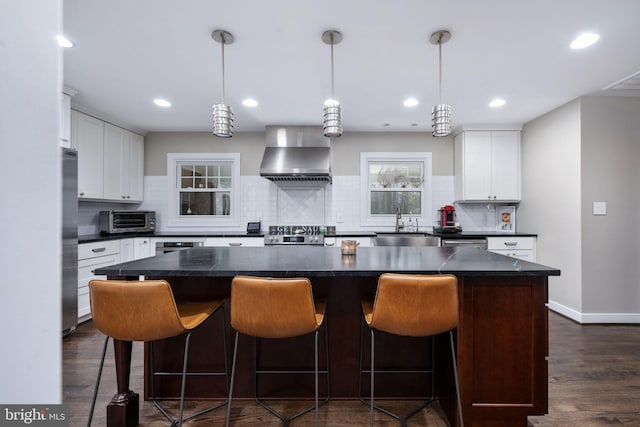 kitchen with dark hardwood / wood-style flooring, wall chimney exhaust hood, decorative light fixtures, a center island, and white cabinetry