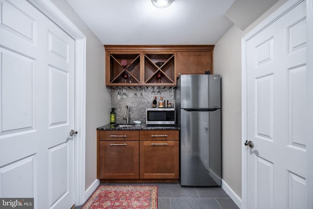 bar featuring sink, stainless steel appliances, dark stone counters, decorative backsplash, and dark tile patterned flooring