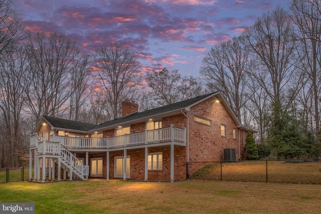 back house at dusk with a lawn, a deck, and central AC