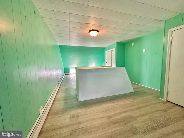 empty room featuring baseboard heating, light hardwood / wood-style flooring, and wooden walls