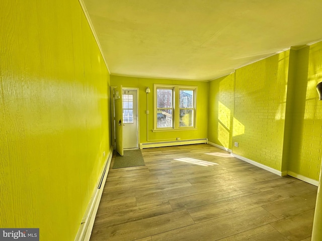 empty room with crown molding, baseboard heating, hardwood / wood-style flooring, and brick wall