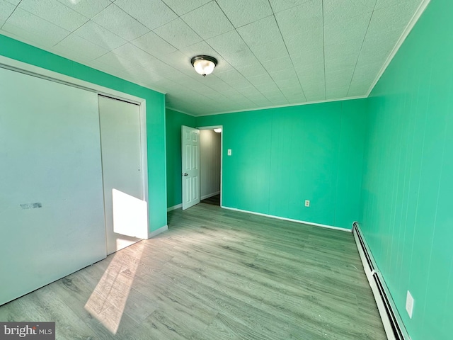 unfurnished bedroom with light wood-type flooring, a closet, and a baseboard heating unit