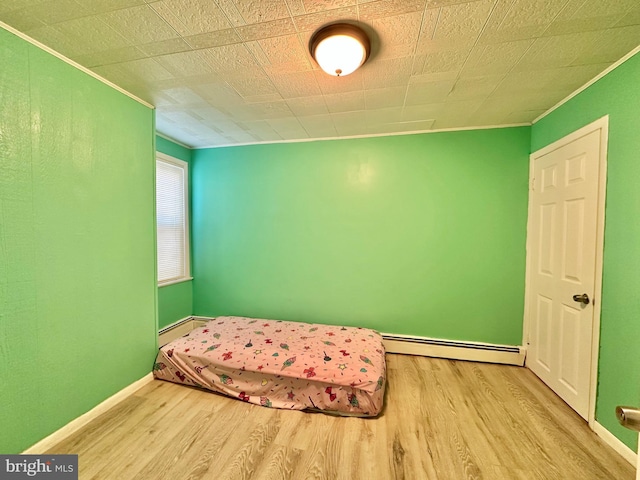 bedroom with a baseboard heating unit and light wood-type flooring