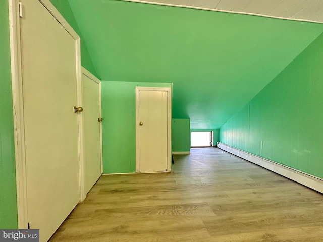 additional living space with a baseboard radiator, light wood-type flooring, and lofted ceiling