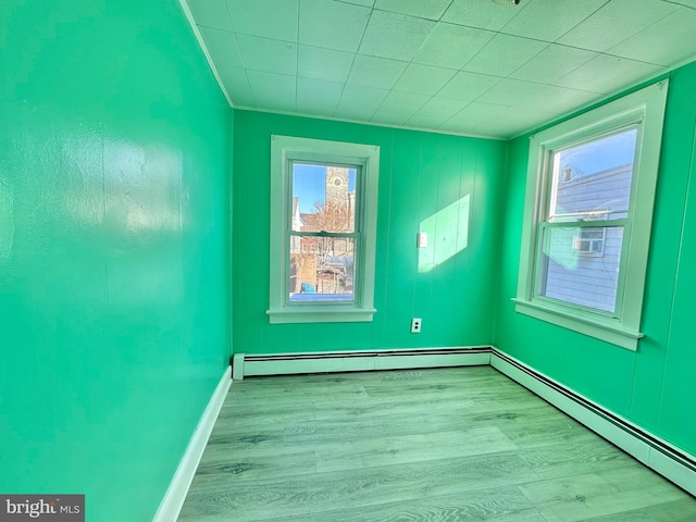 unfurnished room featuring light hardwood / wood-style floors, a baseboard radiator, and a healthy amount of sunlight