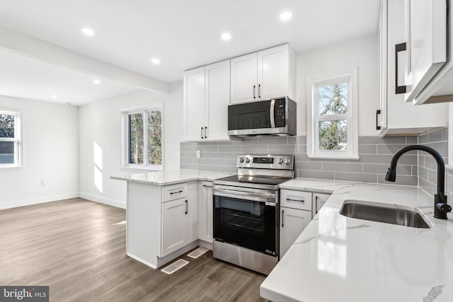 kitchen with sink, appliances with stainless steel finishes, white cabinetry, light stone countertops, and kitchen peninsula