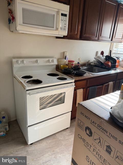 kitchen with dark brown cabinets, white appliances, and sink