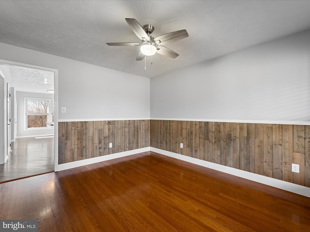 unfurnished room with a textured ceiling, dark hardwood / wood-style flooring, ceiling fan, and wooden walls