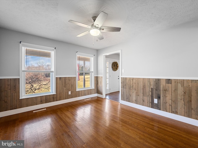 empty room with ceiling fan, dark hardwood / wood-style floors, a textured ceiling, and wooden walls