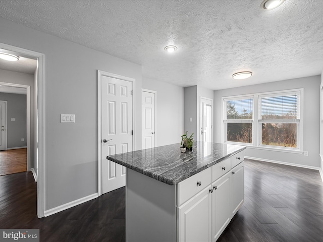 kitchen featuring dark hardwood / wood-style flooring, dark stone counters, a textured ceiling, a kitchen island, and white cabinetry