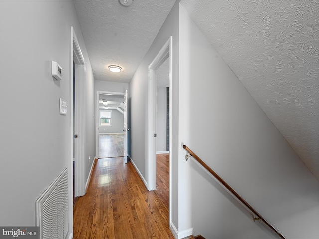 corridor with a textured ceiling and light hardwood / wood-style flooring