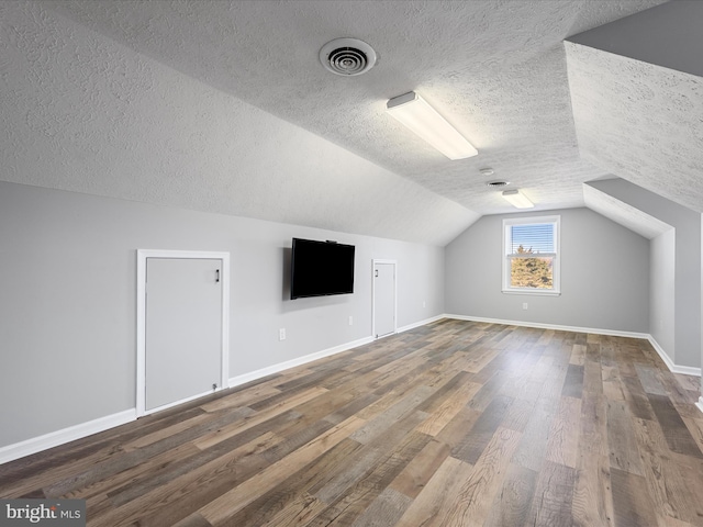 additional living space with a textured ceiling, dark hardwood / wood-style floors, and vaulted ceiling