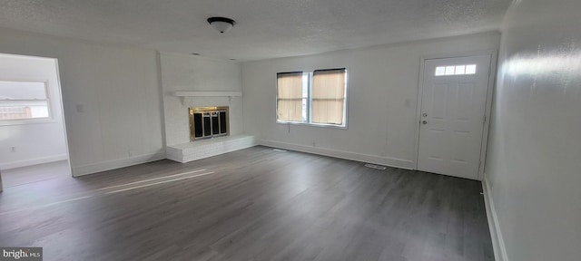 unfurnished living room featuring dark hardwood / wood-style flooring, a wealth of natural light, a fireplace, and a textured ceiling