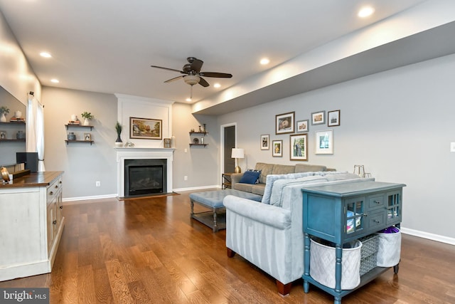 living room featuring ceiling fan, a large fireplace, and dark wood-type flooring