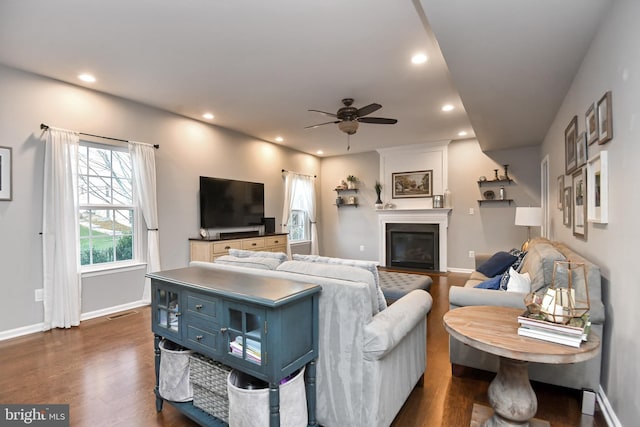 living room featuring ceiling fan, a large fireplace, and dark wood-type flooring