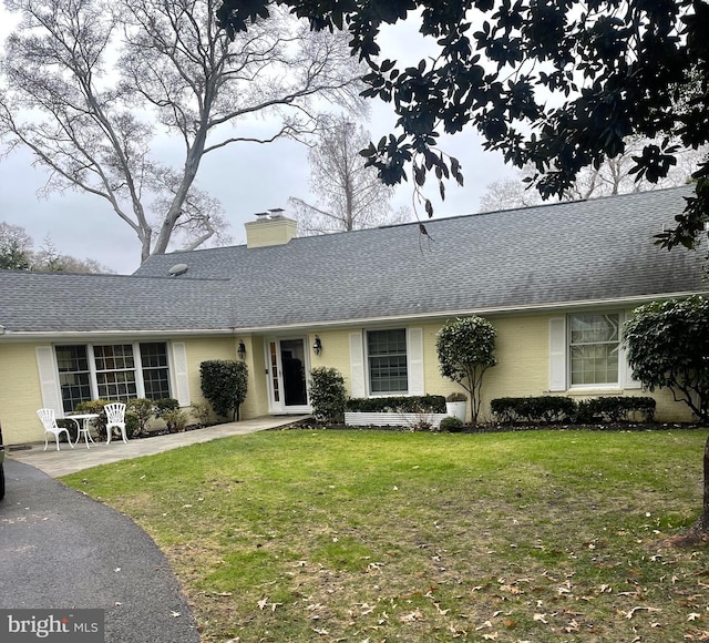 ranch-style house with a chimney, a shingled roof, a front yard, and brick siding