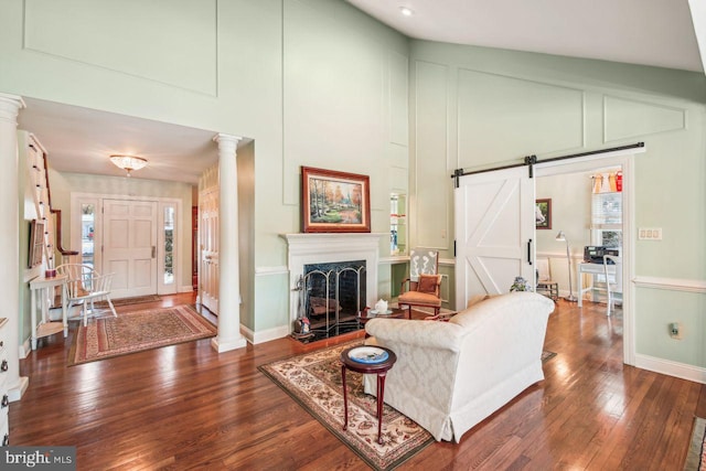 living room with lofted ceiling, a barn door, decorative columns, and dark wood-type flooring