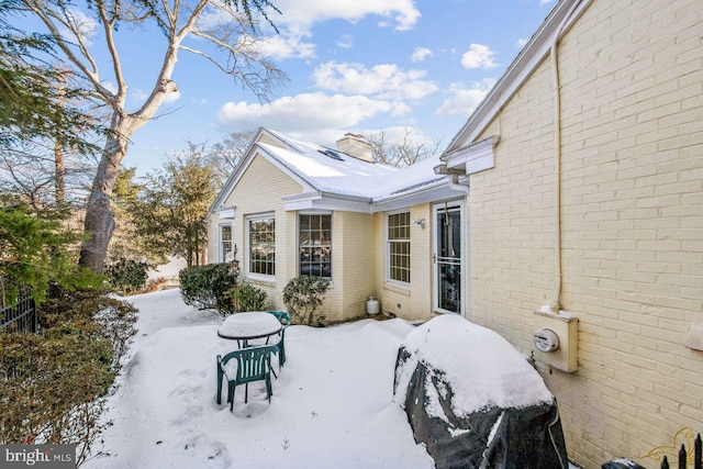 snow covered back of property with brick siding and a chimney