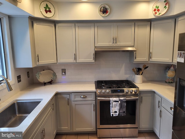 kitchen with stainless steel gas stove, sink, light stone counters, refrigerator, and decorative backsplash