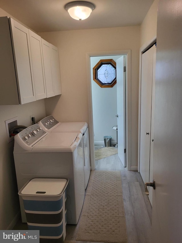 washroom featuring washer and clothes dryer, cabinets, and light wood-type flooring