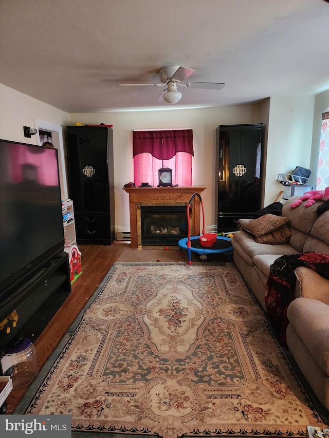 living room featuring a baseboard heating unit, a fireplace, wood finished floors, and a ceiling fan