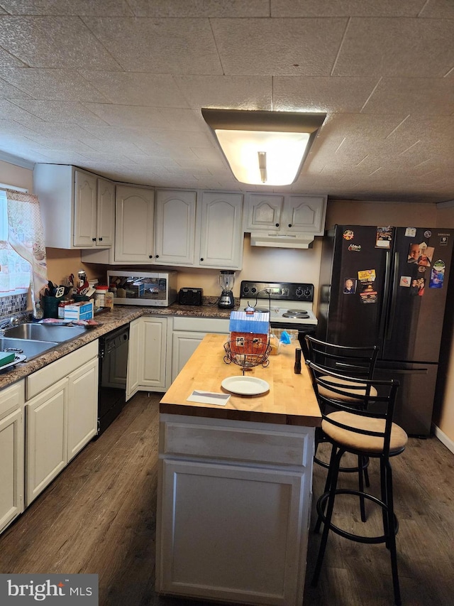 kitchen featuring under cabinet range hood, butcher block countertops, dark wood-style flooring, a kitchen island, and black appliances