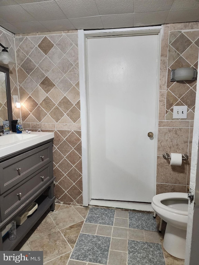 bathroom featuring toilet, vanity, and tile walls