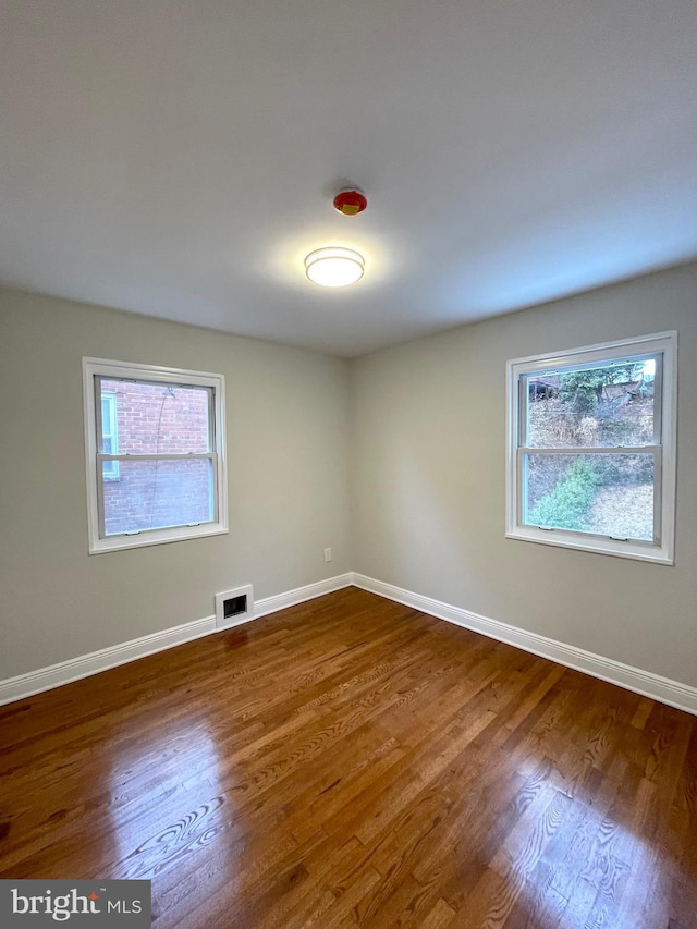 empty room with dark wood-type flooring, plenty of natural light, and visible vents