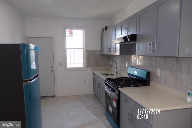 kitchen featuring gray cabinetry, sink, black gas range oven, refrigerator, and decorative backsplash