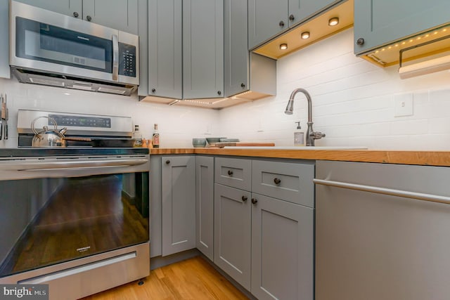 kitchen with appliances with stainless steel finishes, light wood-type flooring, backsplash, sink, and butcher block counters