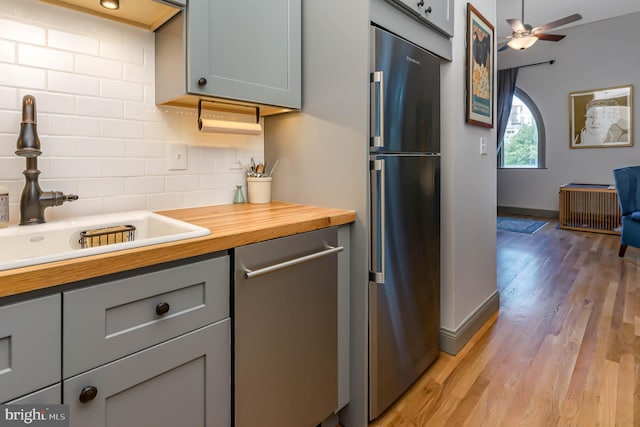 kitchen featuring butcher block counters, sink, stainless steel appliances, light hardwood / wood-style flooring, and backsplash