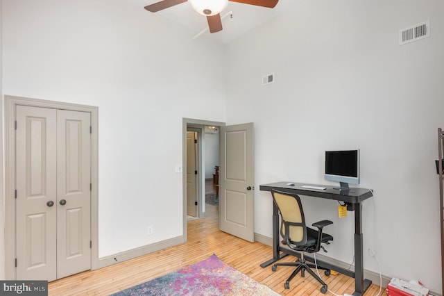 home office featuring light wood-type flooring, a towering ceiling, and ceiling fan