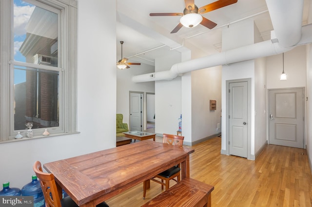 dining room with ceiling fan, a towering ceiling, and light hardwood / wood-style floors