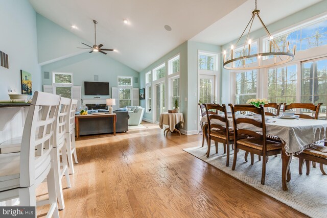 dining space with a high ceiling, ceiling fan with notable chandelier, light hardwood / wood-style flooring, and a wealth of natural light