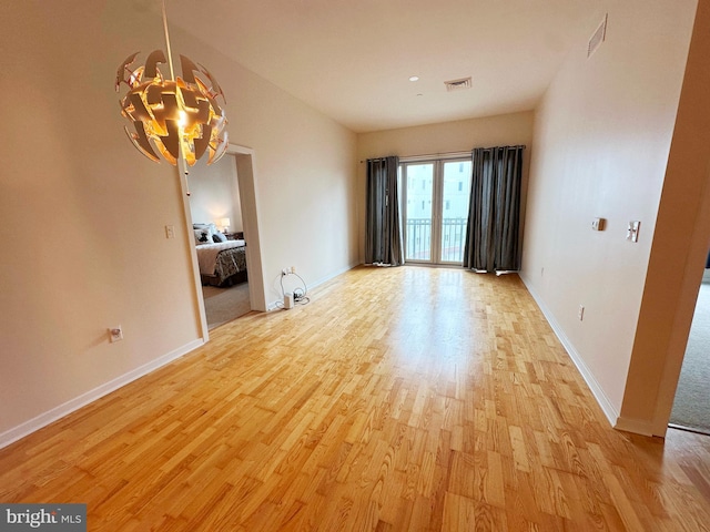 empty room featuring light wood-type flooring and a notable chandelier