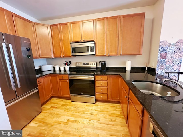 kitchen with light wood-type flooring, stainless steel appliances, dark stone counters, and sink