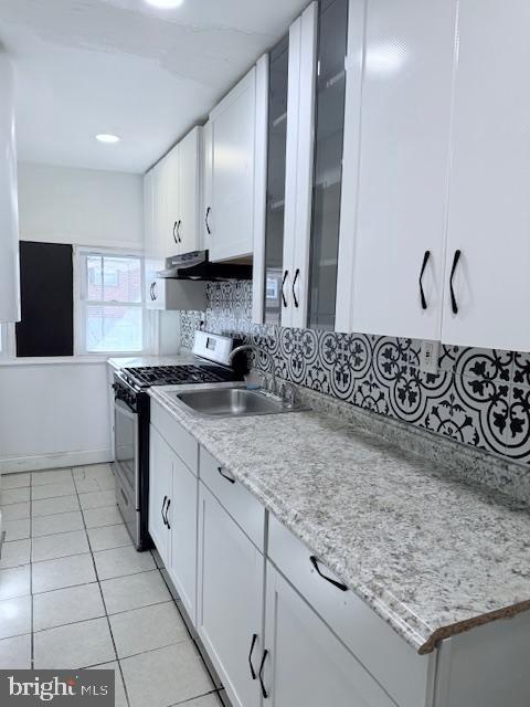 kitchen featuring backsplash, gas range, sink, light tile patterned floors, and white cabinetry