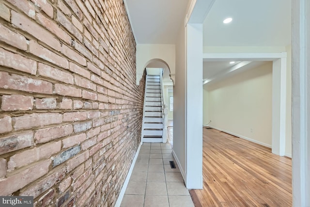 hall featuring light tile patterned floors and brick wall