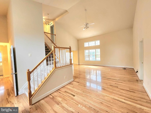 unfurnished living room with high vaulted ceiling, ceiling fan with notable chandelier, and light wood-type flooring